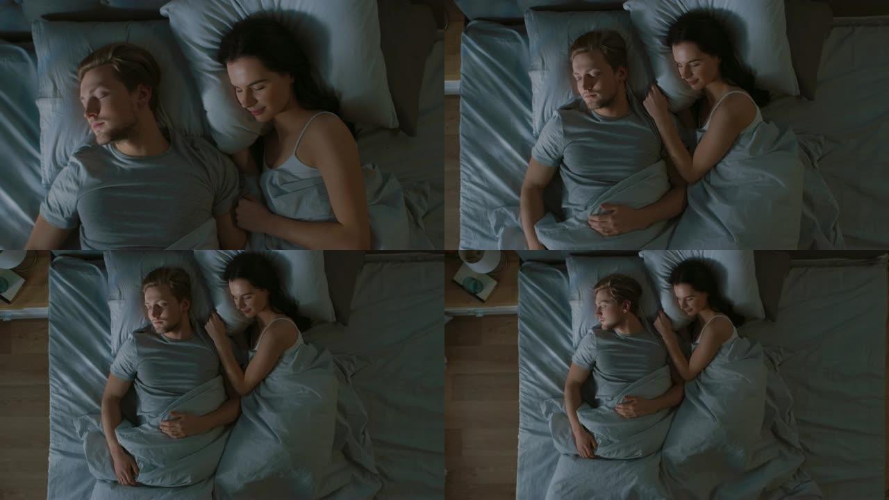 晚上的俯视图床: 迷人的年轻夫妇睡在一起，互相拥抱。早晨的第一缕阳光照亮了窗户的房间