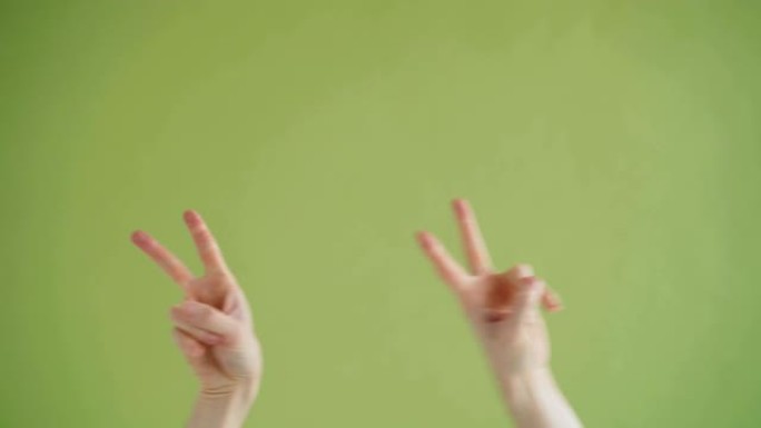 人类双手在绿色背景上制作v形标志移动舞蹈的特写镜头