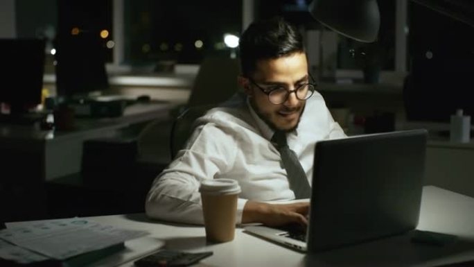 戴眼镜的商人晚上在办公室的笔记本电脑上工作