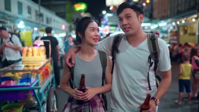 慢动作-旅行者背包客亚洲夫妇在泰国曼谷旅行，甜蜜的夫妇在考山路闲逛时喝酒或啤酒。夫妇在泰国旅游的概念