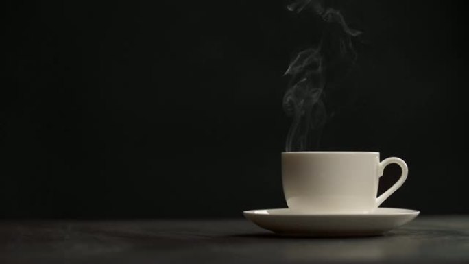 黑色背景上热气腾腾的咖啡杯。一杯最辣的白咖啡慢慢喷出蒸汽。慢动作镜头