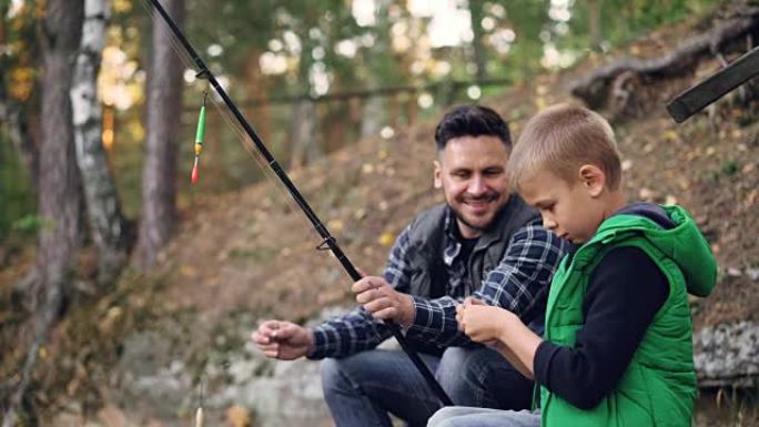 父亲和儿子在钓鱼，拿着鱼竿说话，男人在秋天的日子里教小男孩使用设备，周围有树木。家庭、爱好和休闲概念