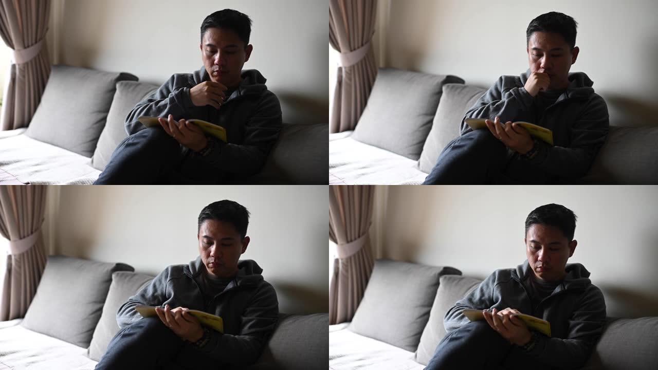 一名亚洲华裔中年男子下午在客厅沙发上看书