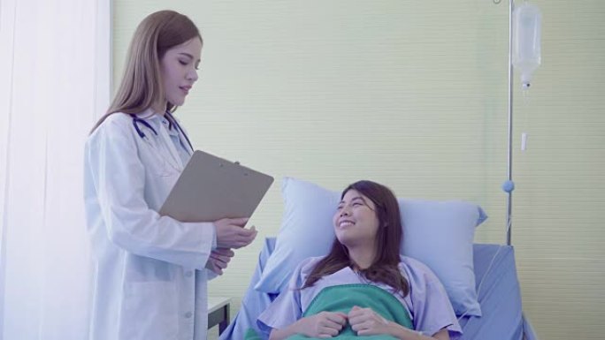 美丽聪明的亚洲医生和病人讨论和解释与医生手中的剪贴板而在病人的病床上在医院。医学保健理念。
