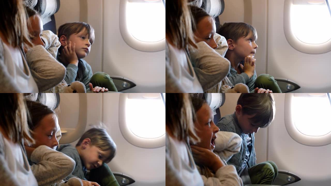 可爱的小男孩很无聊，在与家人一起的长假飞行中，坐在飞机靠窗的座位上四处走动。
