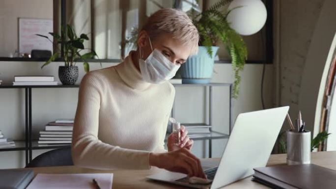 女商人戴着医用口罩清洁笔记本电脑键盘，带消毒剂