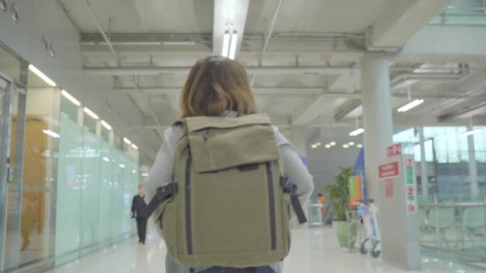 年轻的亚洲背包客女游客在国际机场登机口登机时走在航站楼大厅。生活方式背包旅游度假概念。