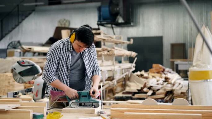 在工厂工作的带砂光机抛光木材的男性木匠的缩小