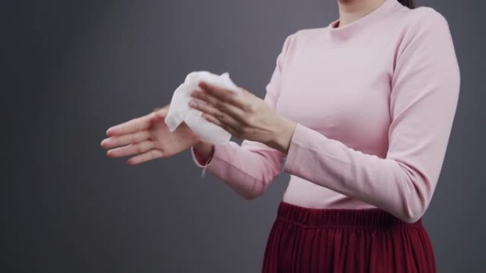 亚洲妇女用婴儿擦纸清洁她的脏手。成年妇女用白色湿纸巾清理她的手。带有复制空间的灰色背景上的医疗保健，