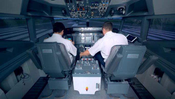 两名飞行员检查驾驶舱中的设备，后视图。