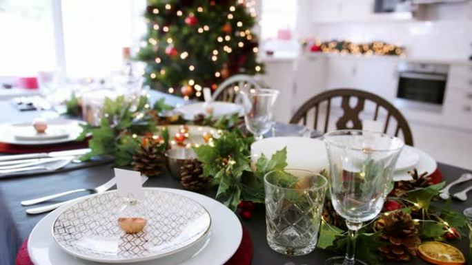 一个特写，缓慢的平移镜头，显示了一个节日的圣诞节餐桌，盘子上摆着摆设的名片持有人，绿色和红色的季节性