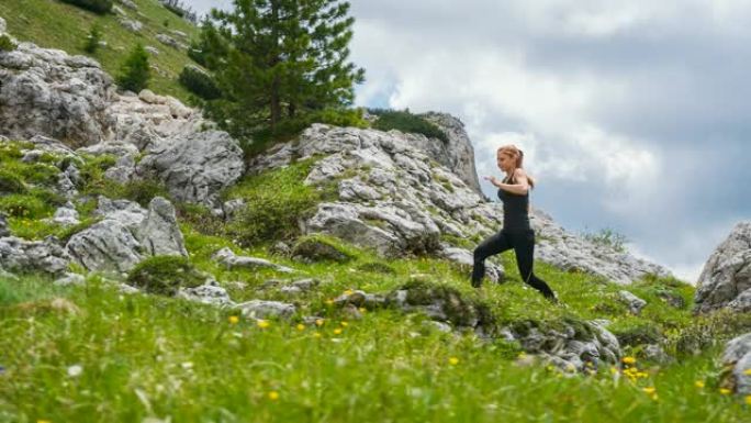 专注的女运动员在山区的岩石小径和草坡上奔跑