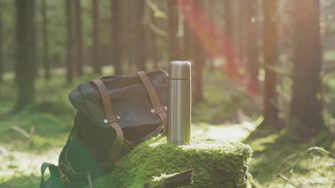 一个不锈钢咖啡热水瓶和一个在森林里的背包