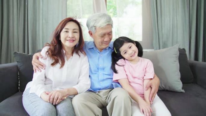 慢动作: 亚洲祖父母和孙女坐在沙发上，看着相机感到高兴。
