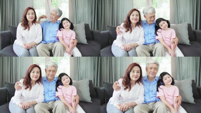 慢动作: 亚洲祖父母和孙女坐在沙发上，看着相机感到高兴。