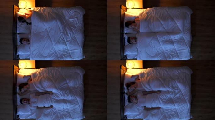 幸福的夫妻在床上醒来。晚上。从上方观看