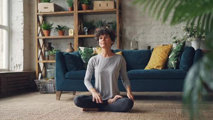 美丽的女人正在完成她的瑜伽练习，并在莲花位置放松，双手放在膝盖上呼吸并享受放松。冥想和运动概念。