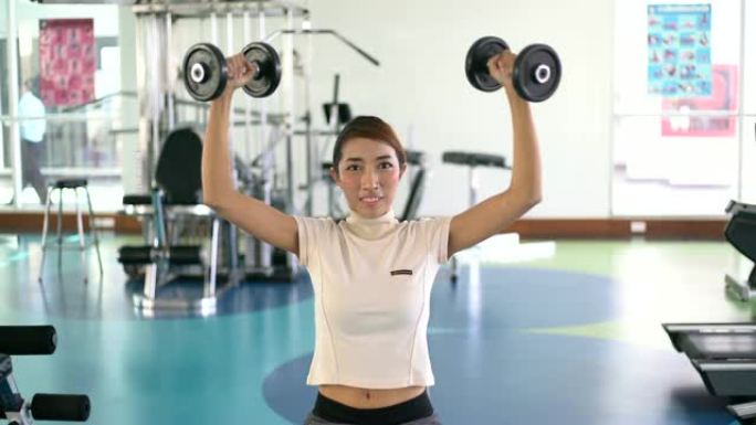 年轻的亚洲妇女在健身房举重，举起哑铃