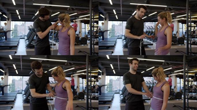 男性私人教练测量在健身房训练的年轻女子的手臂和腰部