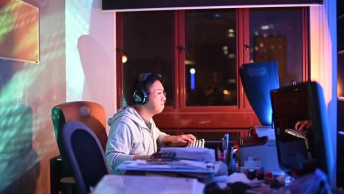 一名亚洲中国中年男性在家在书房玩电脑游戏，耳机在线与队友交谈