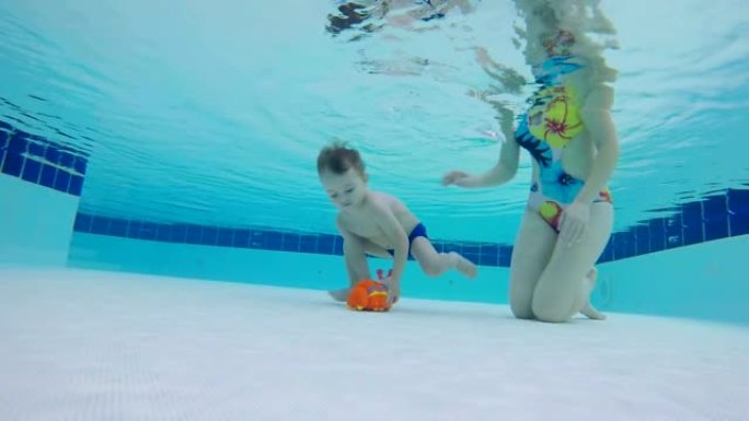 女人帮助孩子从游泳池底部举起玩具