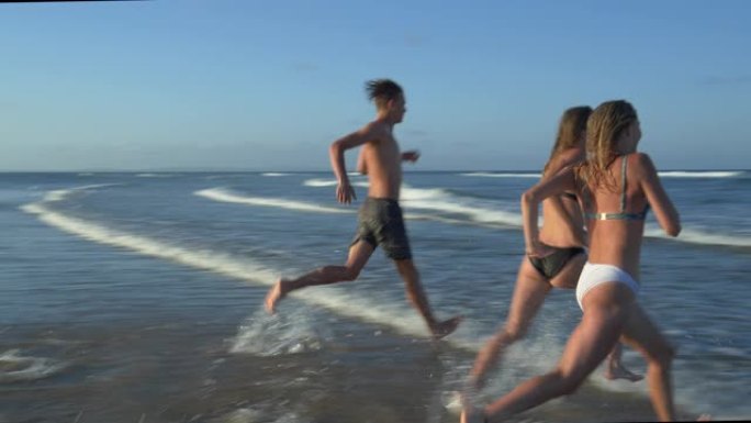 南非，两个美丽的年轻女子和一个年轻男子笑着跑出大海的4k后视图
