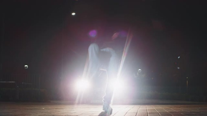 年轻的霹雳舞的慢动作很有趣，晚上在城市停车场用车灯跳舞