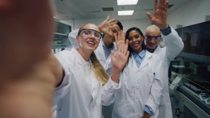 一群戴着防护眼镜的科学家正在对同事进行视频通话或自拍，他们对实验室完成的研究成果感到满意