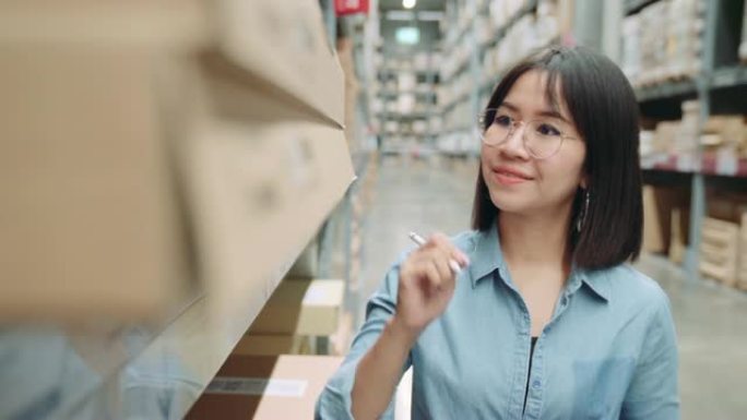 年轻的亚洲老板商人或工人在仓库里用数字平板电脑计算库存。女性企业家在仓库里计算库存。