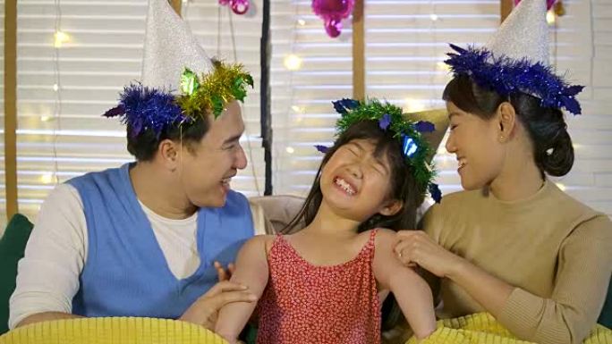 年轻亚洲家庭在家沙发上放松的肖像。父母用爱亲吻他们的女儿。幸福的家庭一起享受时光。