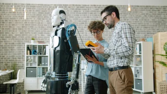 几个开发人员使用平板电脑在现代办公室中测试类人机器人