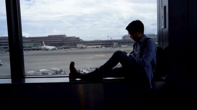 SLO MO Tilt up射击了坐在机场航站楼等待飞机飞行的亚洲男子