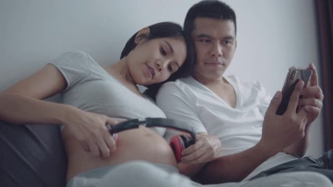 怀孕的夫妇通过耳机为未出生的婴儿播放音乐