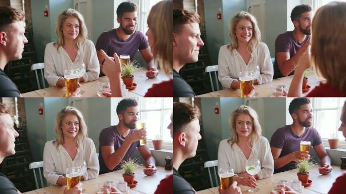 四位年轻的成年同事坐在桌子旁，在酒吧里喝酒和聊天的特写镜头