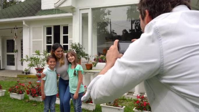 父亲给妻子和两个孩子拍照，他们站在新家外面，都微笑着