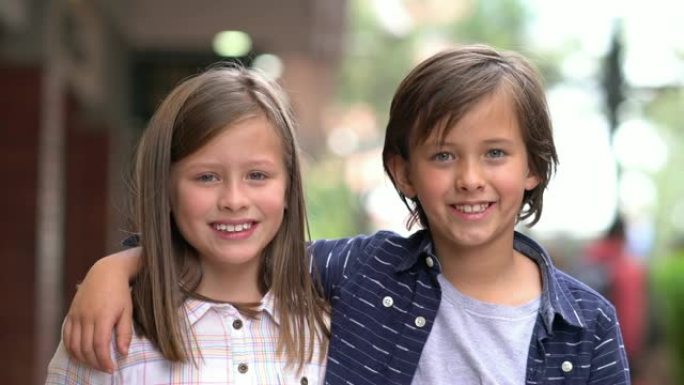 可爱的小弟弟和妹妹在商场对着镜头微笑，同时把头靠在一起