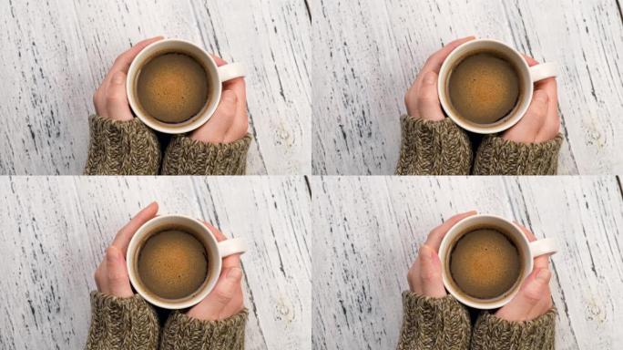 女人喝咖啡，温暖双手。穿着毛衣的女性手拿着一杯早间咖啡。破旧的白色乡村背景