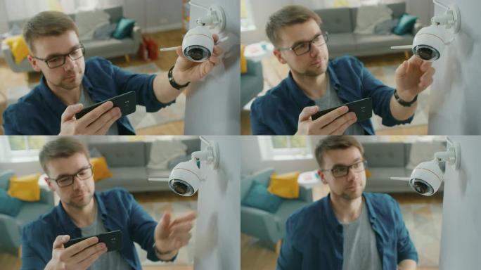 戴着眼镜的年轻人穿着蓝色衬衫，正在家里的白色墙壁上调整带有两个天线的现代wi-fi监控摄像头。他正在