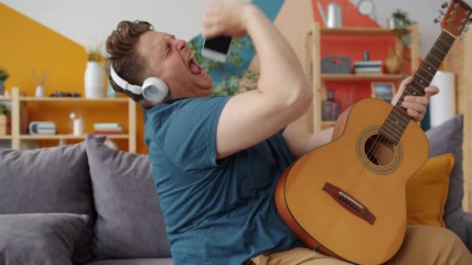 男人在家里戴着耳机在智能手机中弹吉他唱歌的慢动作