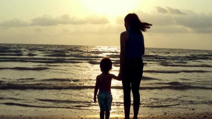 剪影: 妈妈和儿子在沙滩上放松。