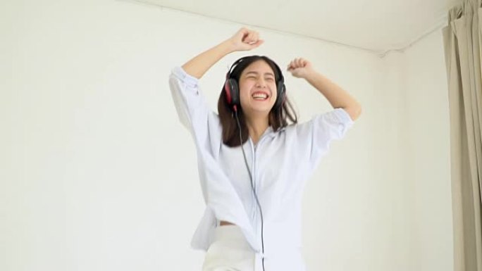 慢动作; 亚洲女孩戴着耳机听音乐，在卧室跳舞。