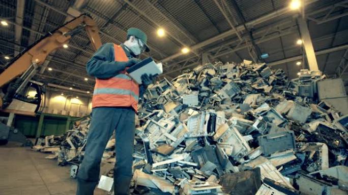 废弃的电子产品和一名垃圾填埋场工人正在检查它