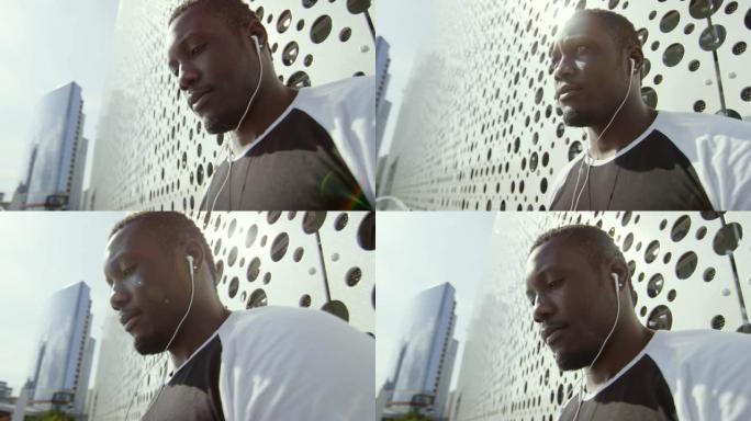 非洲男子戴着耳机在户外穿墙听音乐