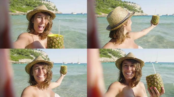 美丽的年轻女孩在海边喝菠萝鸡尾酒，穿着白色帽子的泳衣，金色的沙子，大海的背景。