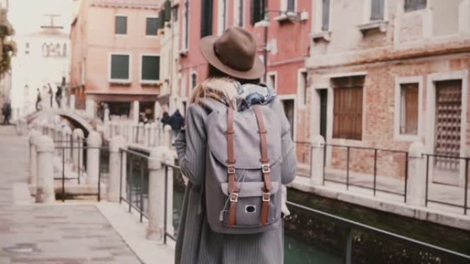 快乐美丽的女游客喜欢沿着意大利威尼斯的水渠街散步，慢动作。