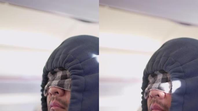 垂直V特写男子在飞机上睡觉，戴着眼罩睡眠面罩和兜帽服装