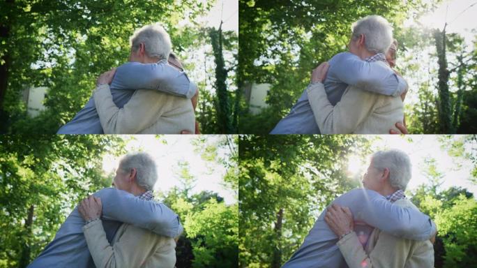 快乐孙子的慢动作在阳光明媚的日子里，在绿色公园里给他的祖父一个情感上的拥抱，以示爱和尊重