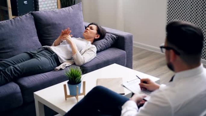 沮丧的女孩与躺在办公室沙发上的心理学家讨论情绪