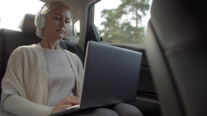 戴着耳机的女人在开车时听音乐和使用笔记本电脑