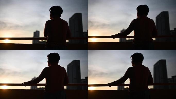 日落时分，亚洲中国中年妇女在阳台上戴着无线耳机听音乐